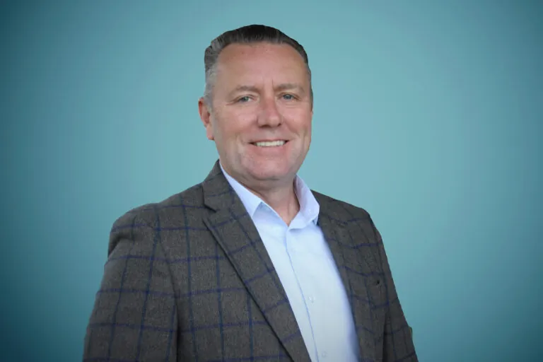 Studio photo of Chris Faber smiling with a teal blue background.